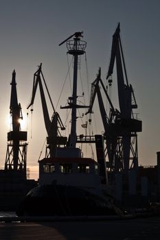 silhouettes of shipyard cranes and tugboat in the evening