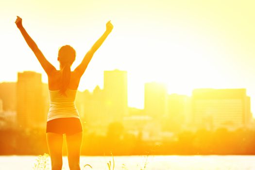 Success winner woman standing with arms up joyful after outdoors workout. Half silhouette on sunny warm summer day with city skyline in background, From Montreal, Quebec, Canada.