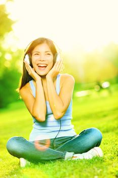 Music headphones woman in park singing listening to music on smart phone or mp3 player in sunshine in park. Mixed race Asian / Caucasian girl smiling happy.