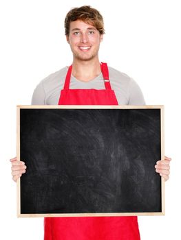 Small business owner showing blank empty blackboard sign wearing apron. Handsome young shop owner man isolated on white background smiling happy.