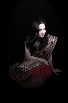 A sad heartbroken Indian royal woman in a traditional red sari and jewelery, on a black studio background.
