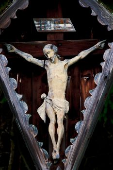 An old and weathered representation of the body of Christ hanging on the cross during the Crucifixion mounted outside.
