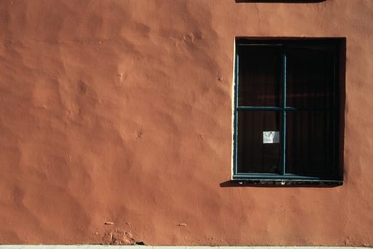 An urban abstract with an orange painted wall, a window with a sign with the words 'WET PAINT'.