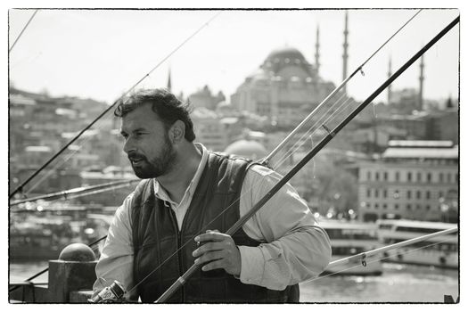 ANGLER GALATA BRIDGE, ISTANBUL, TURKEY, APRIL 15, 2012: Engaged angler at the Galata Bridge on a sunny sunday in April. The Suleymaniye Mosque is seen in the background.