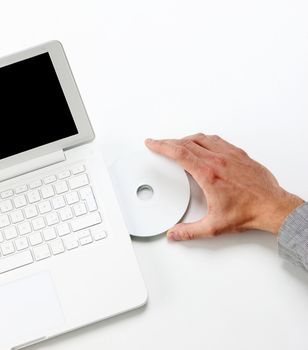 Businessman inserting a cd on white laptop - top view