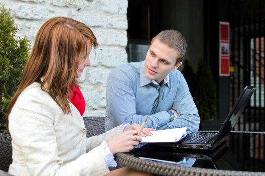 Business partners meeting: Male and female with laptop sitting outdoors