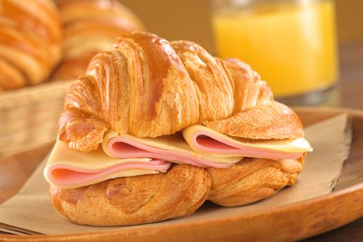 Fresh croissant with ham and cheese on rustic wooden plate with bread basket and juice in the back (Selective Focus, Focus on the ham and cheese slices)