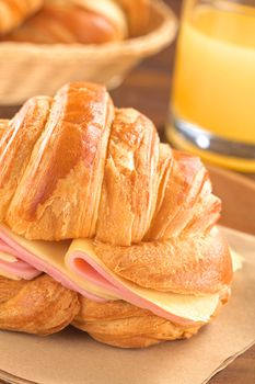 Fresh croissant with ham and cheese slices with juice and bread basket in the back (Selective Focus, Focus on the ham and cheese slices on the right and on the front of the croissant)