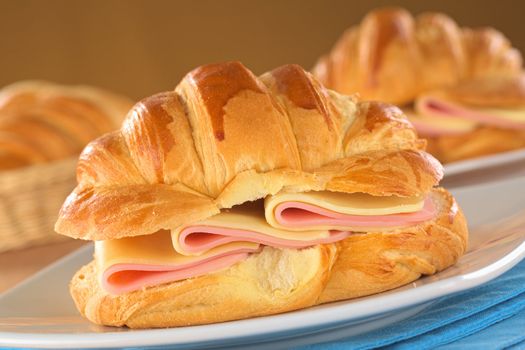 Fresh croissants with ham and cheese on plate (Selective Focus, Focus on the front of the croissant and the ham and cheese slices)