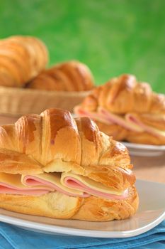 Fresh croissants with ham and cheese on plate with bread basket in the back (Selective Focus, Focus on the front of the croissant and the ham and cheese slices)