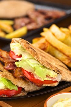 Fresh homemade BLT (bacon lettuce and tomato) wholewheat pita sandwich with French fries on metallic plate with mayonnaise in the front (Selective Focus, Focus on the front of the upper pita stuffing) 