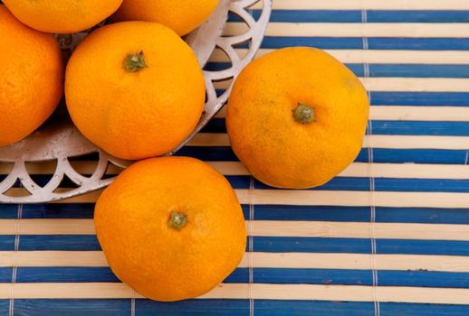 Fresh tangerines on the metal plate and on a white and blue tablecloth