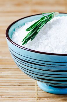 Close up fine sea salt in blue clay bowl on bamboo mat and rosmary