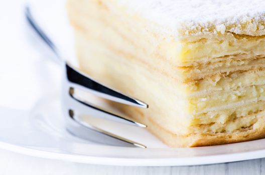 Close up napoleon cake and fork in plate on white table