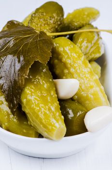 Pickles and garlic in bowl on white wooden table