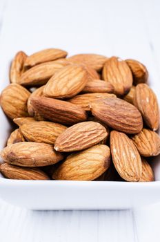 Almonds in a white bowl on white wooden table