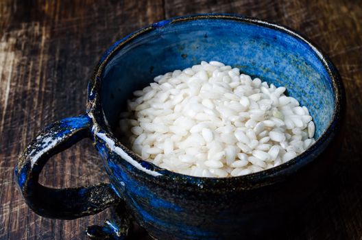 Uncooked risotto rice in blue cup on wooden table