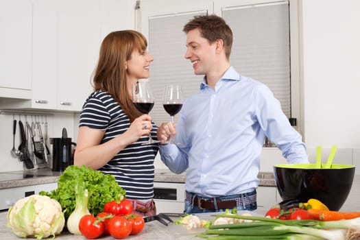 Photo of a young couple preparing salad in their kitchen and drinking wine.