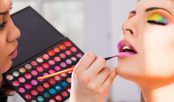 Female make-up artist applying lipstick from colour palette to beautiful woman