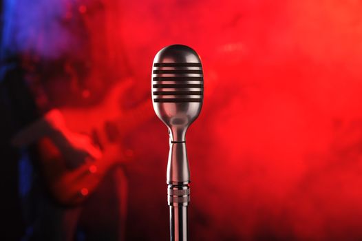 old microphone in the foreground with a guitarist in the background