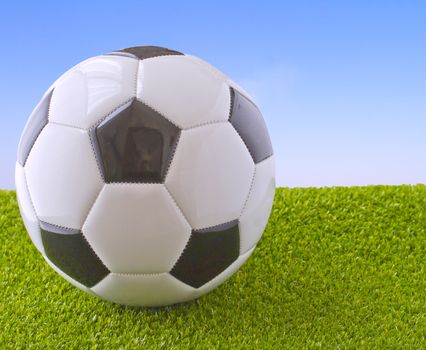 White and black football over grass and blue sky