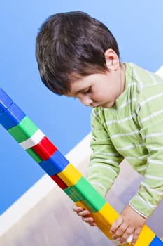 A smiling little boy is building a toy block. Wooden room