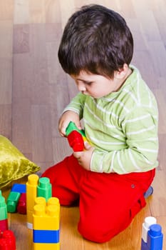 A happy little boy is building a colorful toy block tower