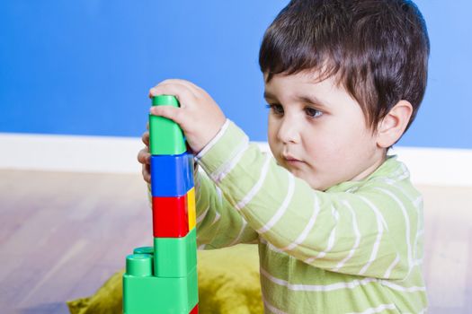 Brunette Baby playing with bright blocks on wooden room