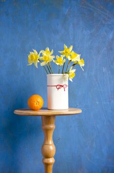 bouquet narcissus in vase and orange fruit on blue background