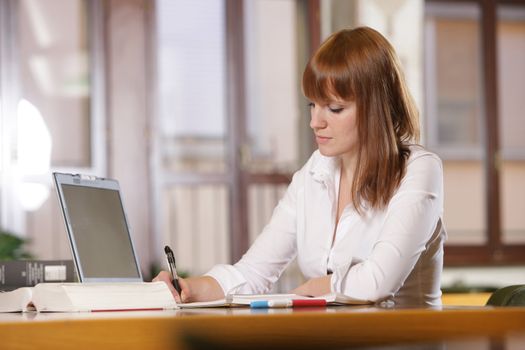 in the library -young female student with laptop and books working in a high school library