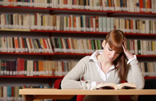 Portrait of a serious young student reading a book in a library 