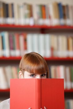 Girl hiding behind the book,  library on background