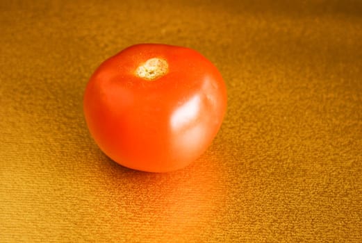 Red tomato on gold background in natural light.