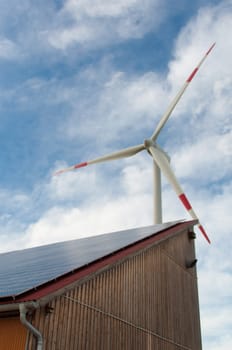 barn covered with solar panels and wind turbine in the background