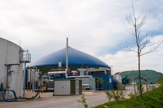 Different fermenters of a biogas plant in front of a cloudy blue sky