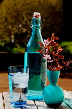 Blue glass with ice water, blue bottle and a blue vase with cherry blossoms outdoor in a garden