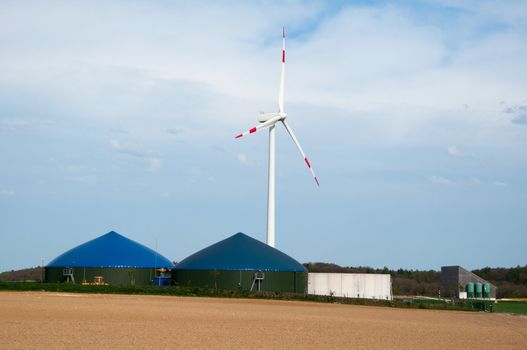 Different fermenters of a biogas plant with windmill in the background