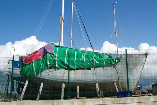 A yacht supported by wooden posts in dry dock under going renovation work with an exposed hull.