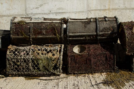 A set of working lobster pots covered with seaweed stacked against a concrete wall and floor.