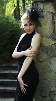 Retro-styled woman in black dress near stone wall