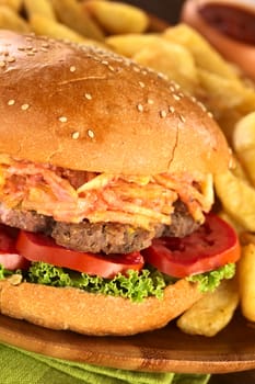 Hamburger with French fries on rustic wooden plate with ketchup (Selective Focus, Focus on the front of the hamburger)