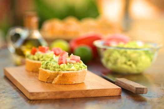 Snack of baguette slices with avocado cream, tomato and onion on wooden cutting board (Selective Focus, Focus on the front of the avocado cream on the first baguette slice)