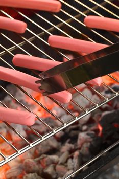 Sausages on barbecue with tongs with glowing charcoal below (Selective Focus, Focus on the end of the tongs and the lower end of the sausage they touch)