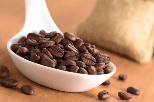 Roasted Peruvian coffee beans on ceramic spoon with jute sack in the back (Selective Focus, Focus on the coffee beans one third into the spoon)