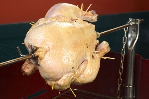 Whole chicken being grilled on spit over a charcoal barbecue (Selective Focus, Focus on the front of the chicken)