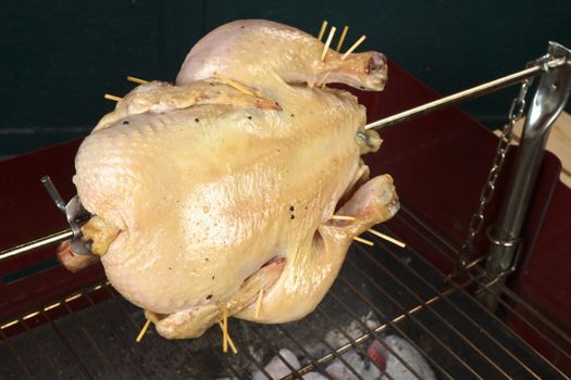 Whole chicken being grilled on spit over a charcoal barbecue (Selective Focus, Focus on the front of the chicken)