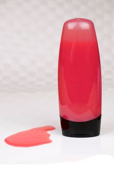 red colored shower gel bottle and squeezed sample on grey background