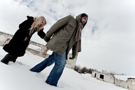 Homeless couple struggle in winter, holding hands and walking through ruins in the snow