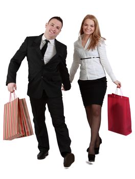 Happy young couple carrying shopping bags and holding their hands, coming through the camera, against a white background.