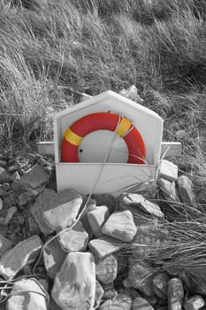 lifebuoy on rocky beal beach in county Kerry Ireland with dunes in background in black and white with buoy still in orange and yellow